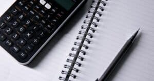 Αριθμομηχανή, τετράδιο και στυλό πάνω σε γραφείο.