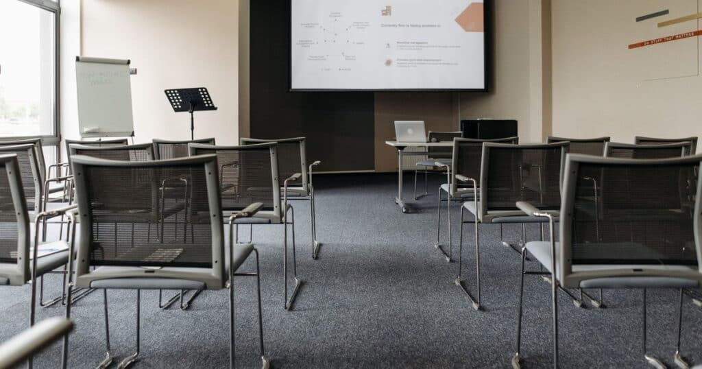 Άδεια καθίσματα σε φωτεινή αίθουσα με οθόνη προβολής.