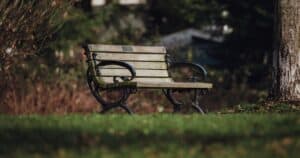 Ξύλινο παγκάκι με μεταλλικά μπράτσα κάτω από δέντρο