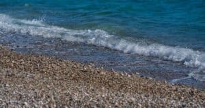 Καθαρά γαλάζια νερά φτάνουν σε ακτή με βότσαλα.