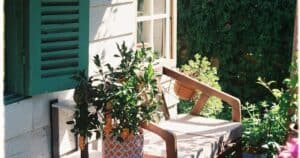 Ξύλινο κάθισμα δίπλα σε πράσινα παντζούρια και γλάστρα.