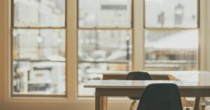 Άδεια γραφεία με καρέκλες μπροστά σε μεγάλα παράθυρα σε απαλό φως.