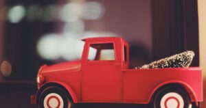 Κόκκινο παιχνίδι φορτηγάκι σε ράφι με θολά φώτα στο βάθος.
