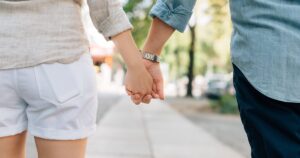 Δύο άνθρωποι περπατούν πιασμένοι χέρι χέρι σε δεντρόφυτο πεζοδρόμιο.