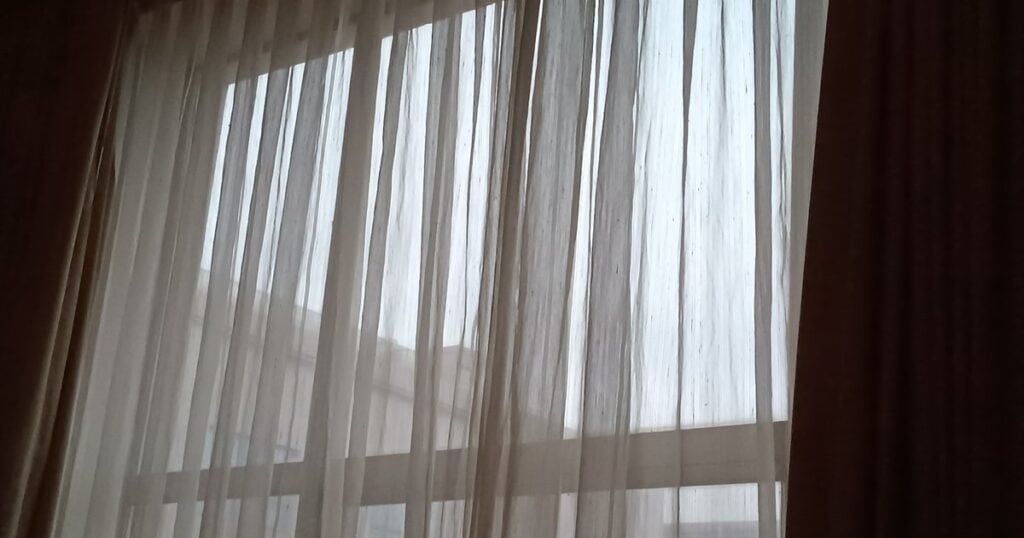 Φως περνά μέσα από λεπτή λευκή κουρτίνα σε μεγάλο παράθυρο.