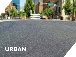 Freshly paved urban asphalt street with city buildings and trees.