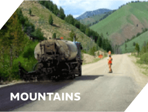 Damaged asphalt road with construction warning signs in mountainous terrain.