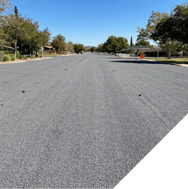 Freshly paved asphalt road with clear blue sky and trees on sides.