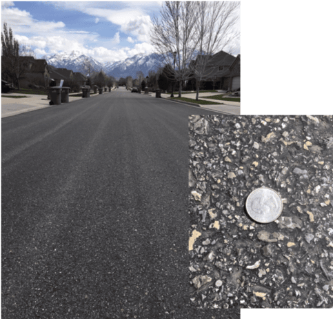 Freshly paved asphalt street with gravel close-up and mountain view in background.