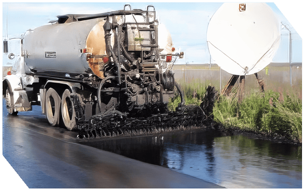 Asphalt paving truck applying fresh asphalt on road surface.