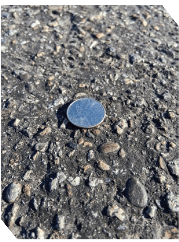 Close-up of asphalt surface with a coin for size reference.
