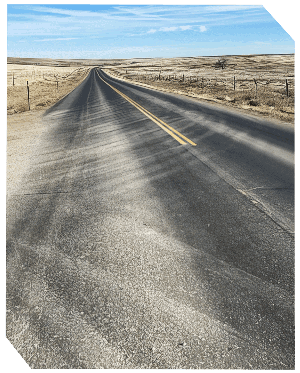 Newly paved asphalt road stretching through open rural landscape.