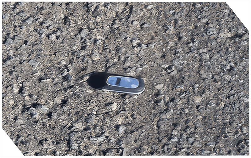 Close-up of asphalt surface with a small inspection device.