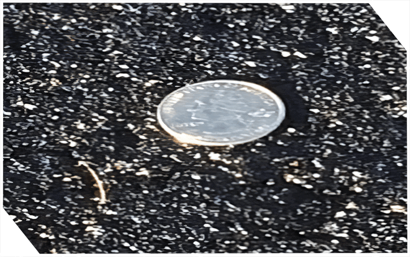 Close-up of a coin embedded in asphalt surface for repair testing.