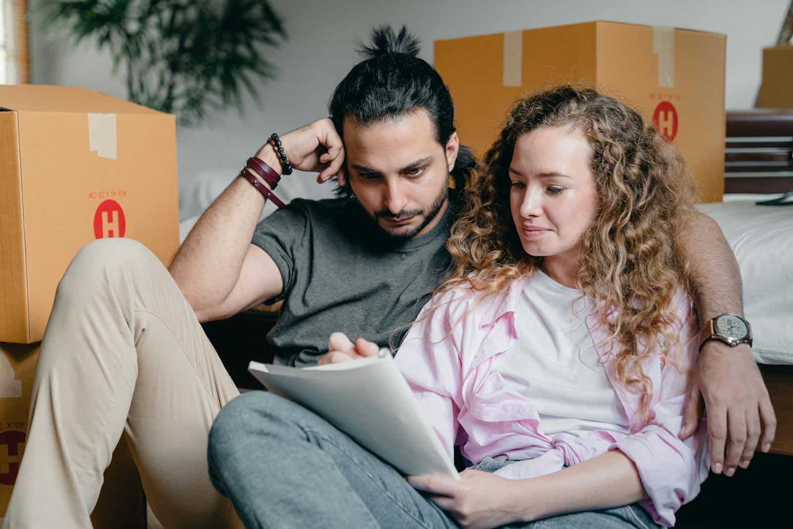 Horoscope, reading, success, astrology, Pensive male and female in casual clothes sitting together among boxes and writing notes in notebook while leaning on bed