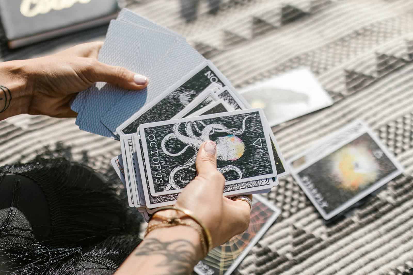 Horoscope Predictions, Hands holding tarot cards during a reading session on a patterned mat.