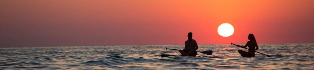 Silhouette of a couple paddleboarding on the ocean during a stunning sunset, capturing romance and adventure.