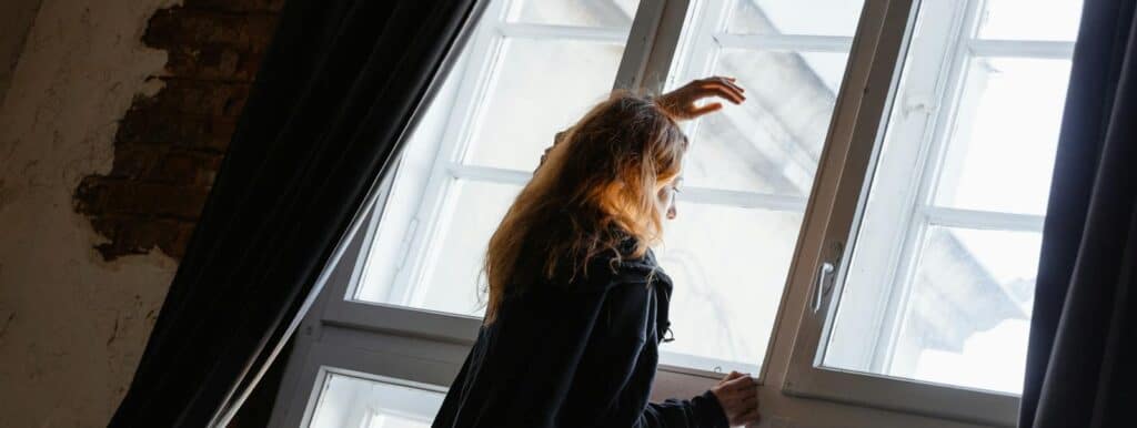 A woman stands in deep thought near a large window, embracing solitude. Jyotish Natal Chart navigating life challenges
