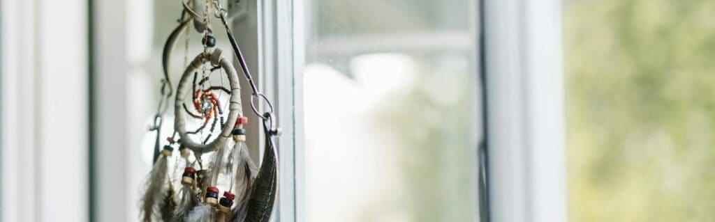 A dreamcatcher with feathers hangs by a sunlit window, creating a serene ambiance. Dreams, astrology, moon cycles