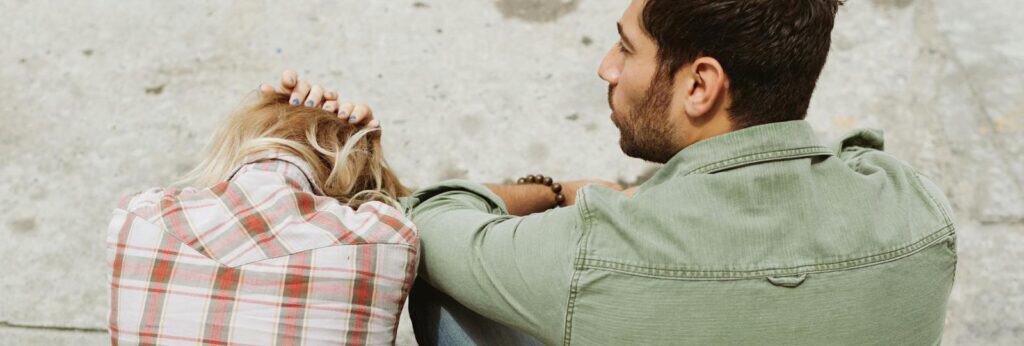 A couple sitting on the street, engaged in a distressed conversation, capturing a moment of emotional tension.
