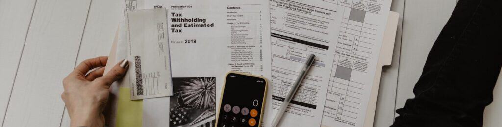 person holding paper near pen and calculator