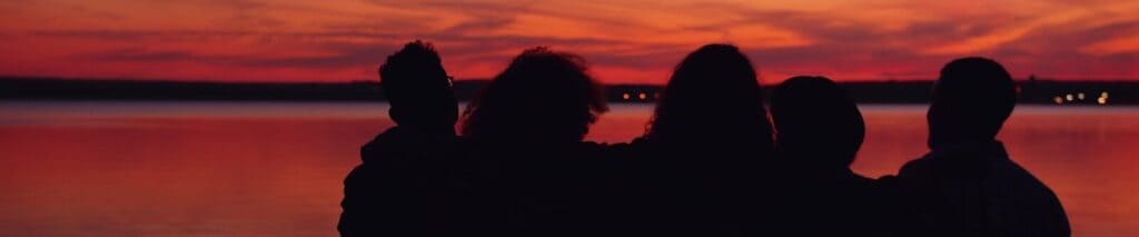 Silhouettes of people watching a vibrant sunset over water.