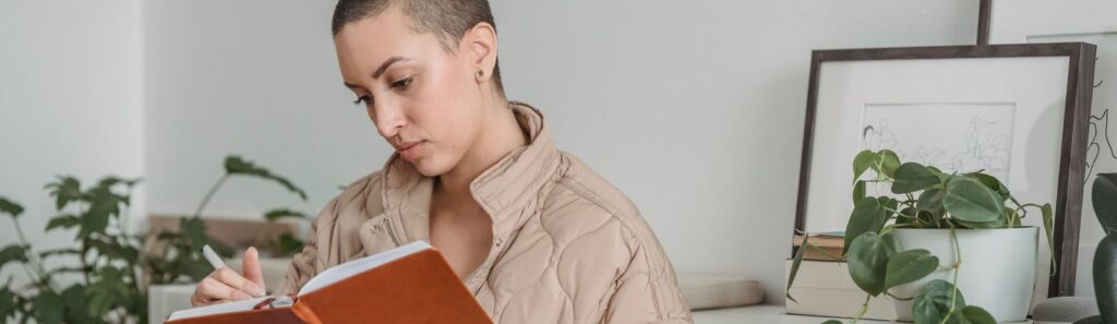 Young female with tattooed ring and short hair taking notes in agenda while sitting in house room