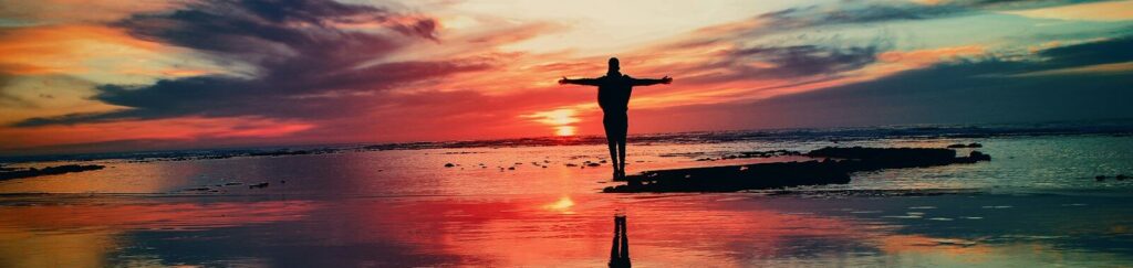 silhouette of person standing on rock surrounded by body of water