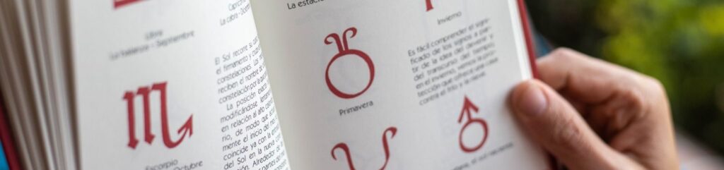 Open book displaying zodiac symbols and seasonal descriptions being held by hands.