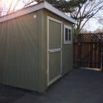 Small green outdoor storage shed with window and door in backyard.