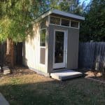 Modern garden shed with large windows and a small porch, situated in a backyard.