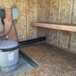 Utility storage shed interior with electrical panels and plumbing connections.