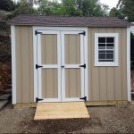 Storage shed with beige siding, white trim, and black hardware, featuring double doors and a small w.