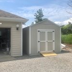 Garden shed with double doors for outdoor storage, placed beside a house in a backyard setting.