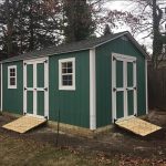 Garden shed with double doors and windows, green exterior, in a backyard setting.