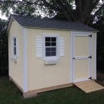 Yellow garden shed with white trim and window shutters.
