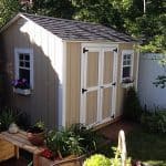 Garden shed with beige exterior, double doors, and decorative window boxes filled with flowers.