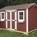 Red garden shed with white trim, double doors, and windows in a backyard setting.