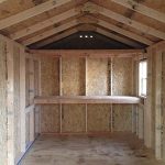 Garden shed interior with wooden walls, ceiling, and built-in shelving for storage.