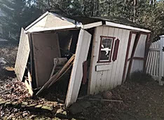 Garden shed with damaged roof and leaning structure.