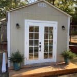 Garden shed with double glass doors, outdoor potted plants, and wooden deck.