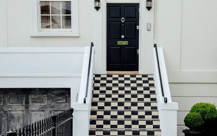A smart entrance door with a modern black-and-white theme, pitch-black door and black-and-white grid tiles on steps.