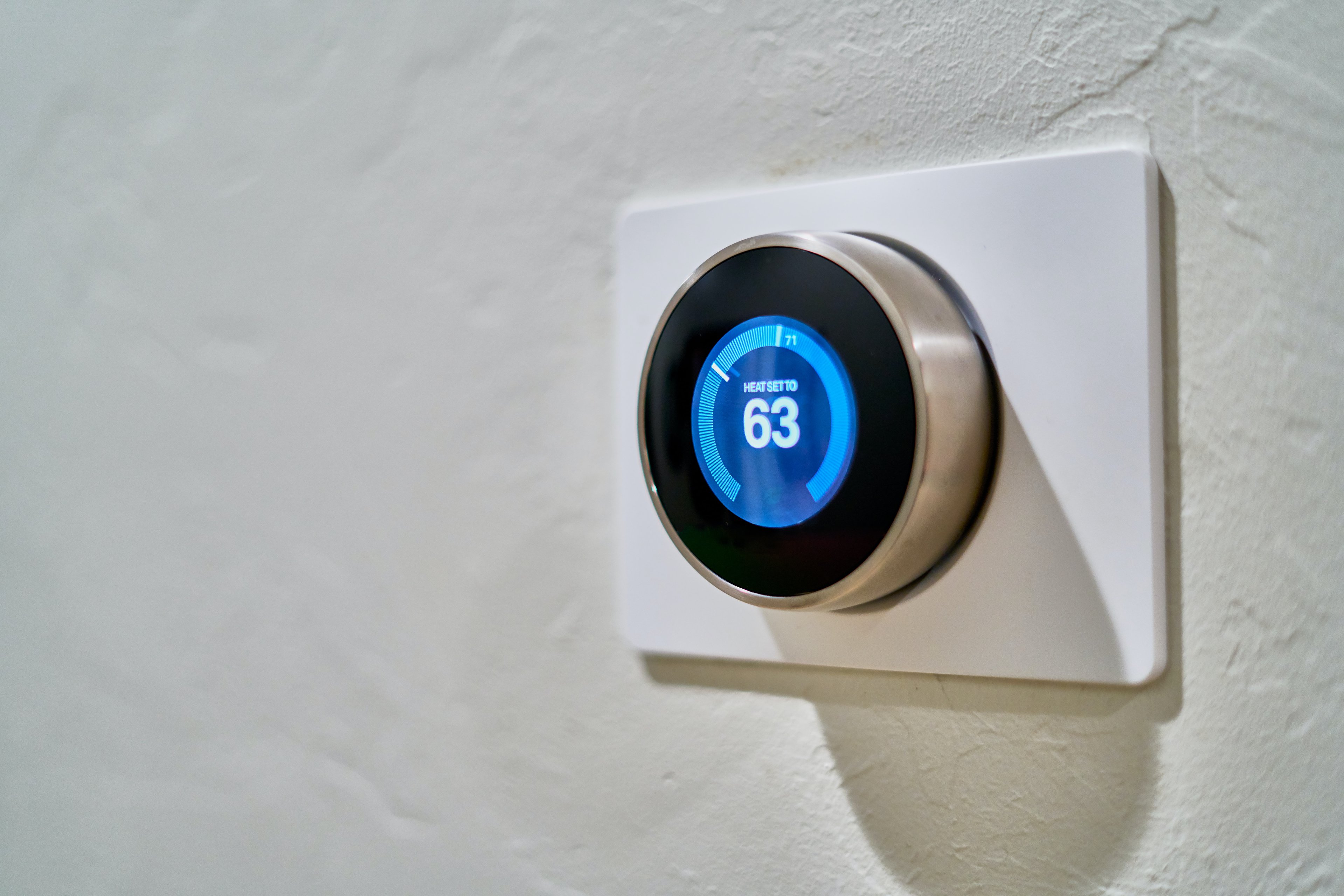 A modern digital thermostat mounted flush to a wall in a residence.