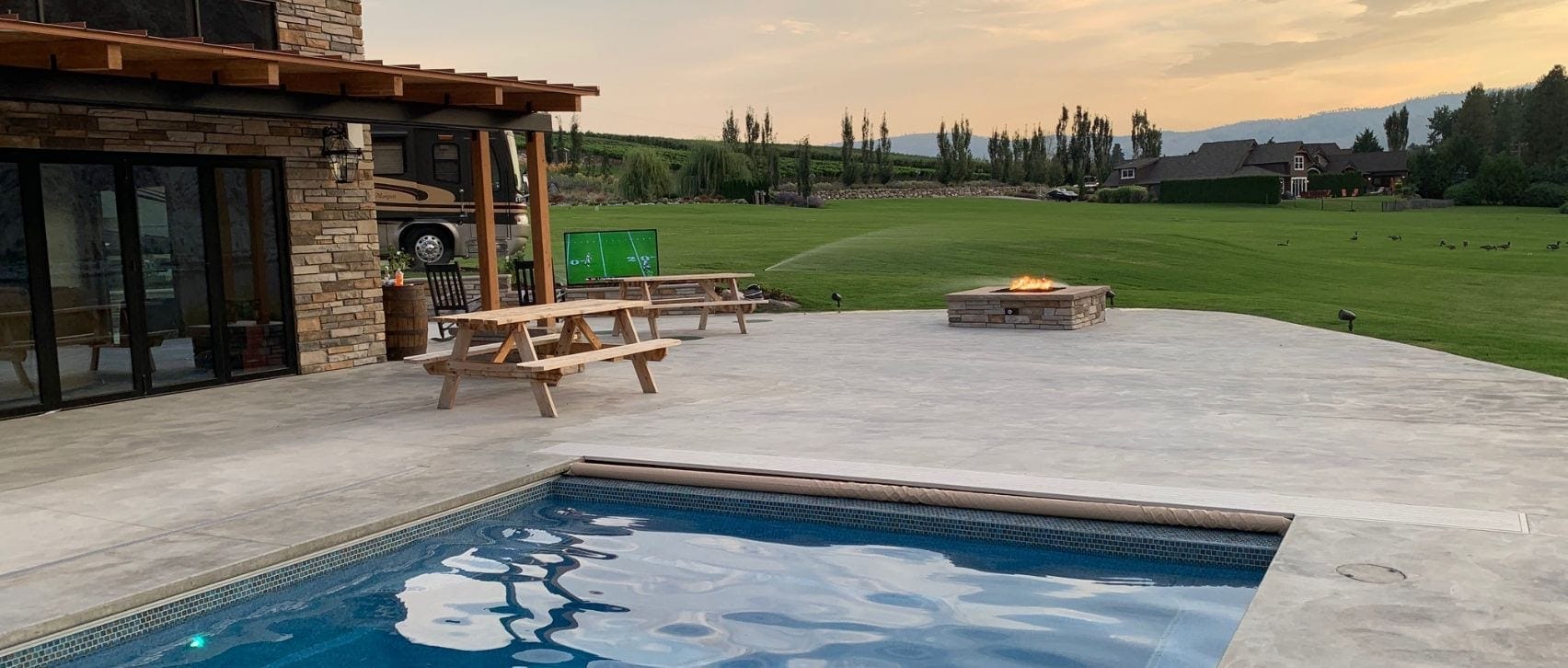 Outdoor AV solutions featuring a backyard poolside entertainment system with TV and fire pit
