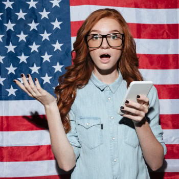 Junge Frau mit Smartphone vor US-Flagge, überrascht und verwirrt.