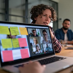 Team-Meeting mit Videoanruf und digitalen Notizen auf Laptop.