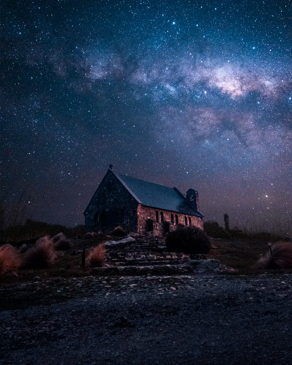 Starry night sky with numerous stars and the Milky Way galaxy visible above a small stone church.