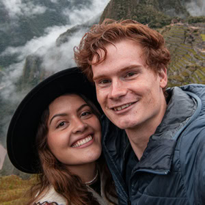 A young couple smiling outdoors near a waterfall in a lush green landscape.