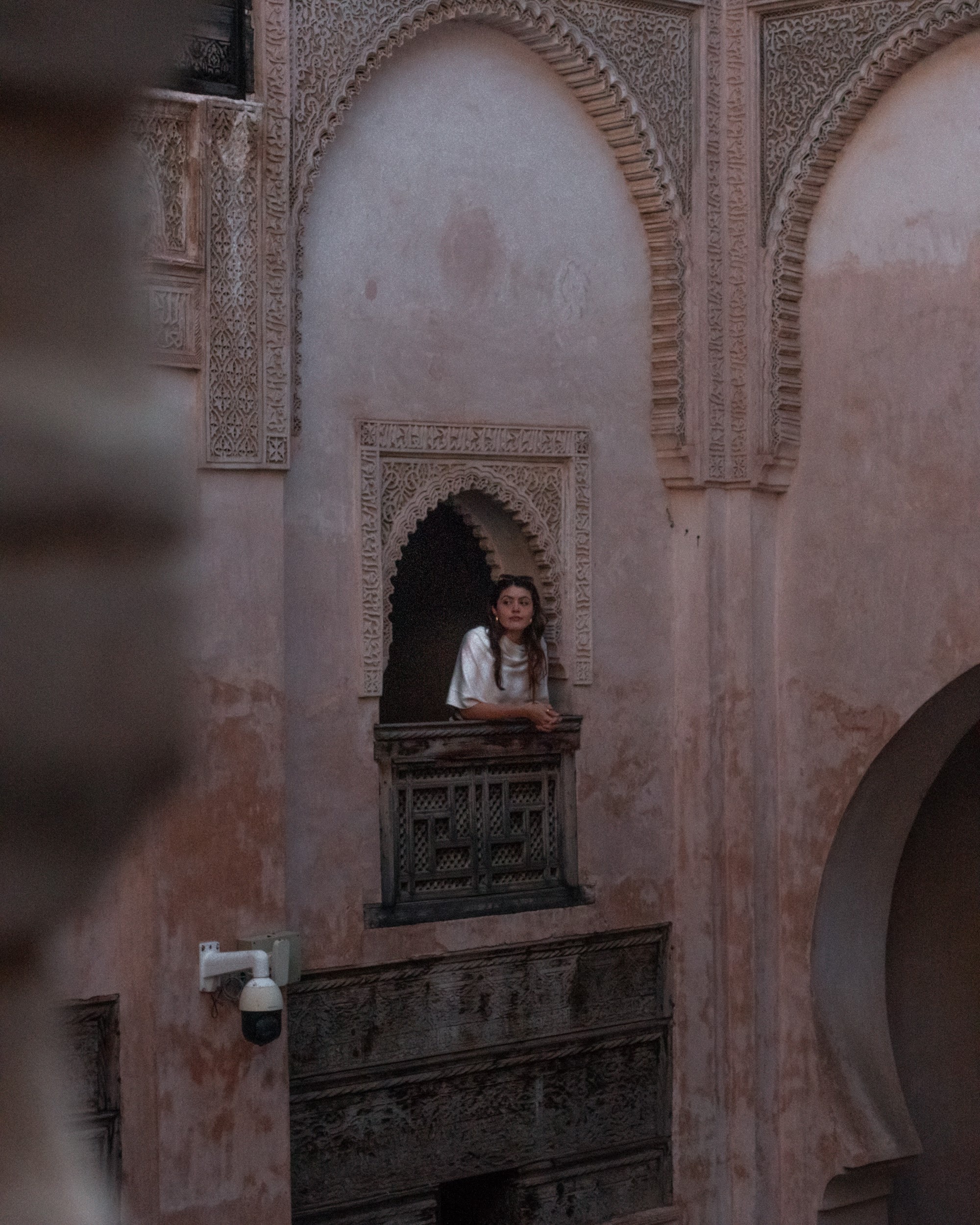 1. Woman with long dark hair in a white shirt leaning on a small ornate balcony.