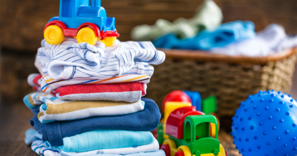 Brightly colored baby clothes and plush toys for infants and toddlers on a wooden surface.